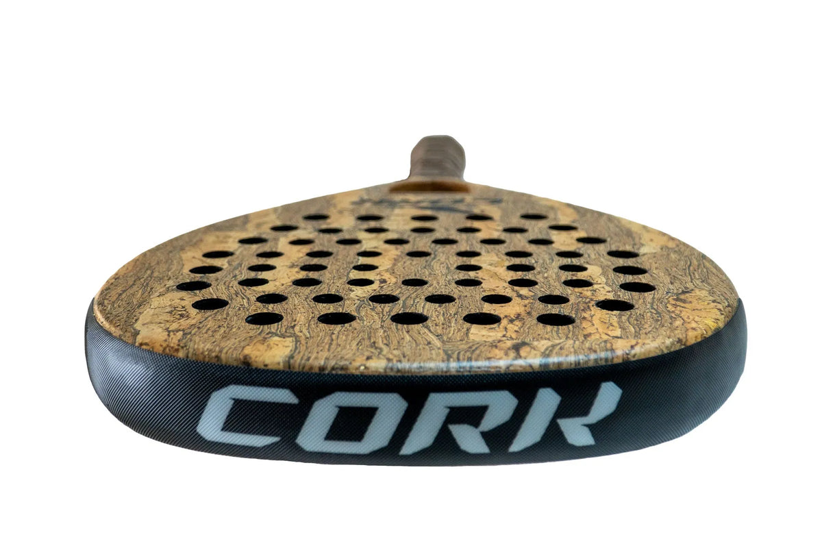 Close-up of a Cork Padel Premium Hybrid III Racket showcasing its cork-textured surface and advanced anti-vibration cap, with a multi-diameter hole pattern. CORK is prominently displayed on the side in large white letters against a plain white background.