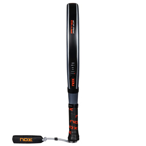 The Nox Padel Racket AT Pro Cup Comfort 25 by Agustín Tapia features a black and red design with photochromic paint and a textured grip, complete with a wrist strap. It includes Fiber Glass Silver technology for enhanced performance.