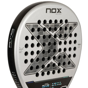 A close-up of the NOX Padel Racket AT10 Genius 18K by Agustin Tapia 2024 reveals a metallic-finished aluminized carbon fiber construction. It features an X pattern, circular holes, branding text, and subtly integrated EOS Flap technology with technical specs on the frame.