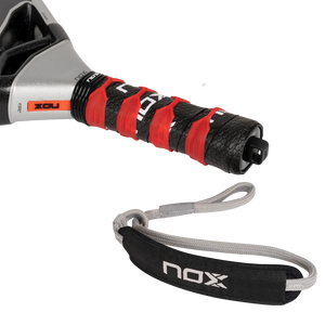 Close-up of the NOX Padel Racket AT10 Genius 18K handle, wrapped in black and red grip tape. Enhanced with EOS Flap technology, it includes a gray wrist strap showing the NOX brand and features a textured, contrasting color design.