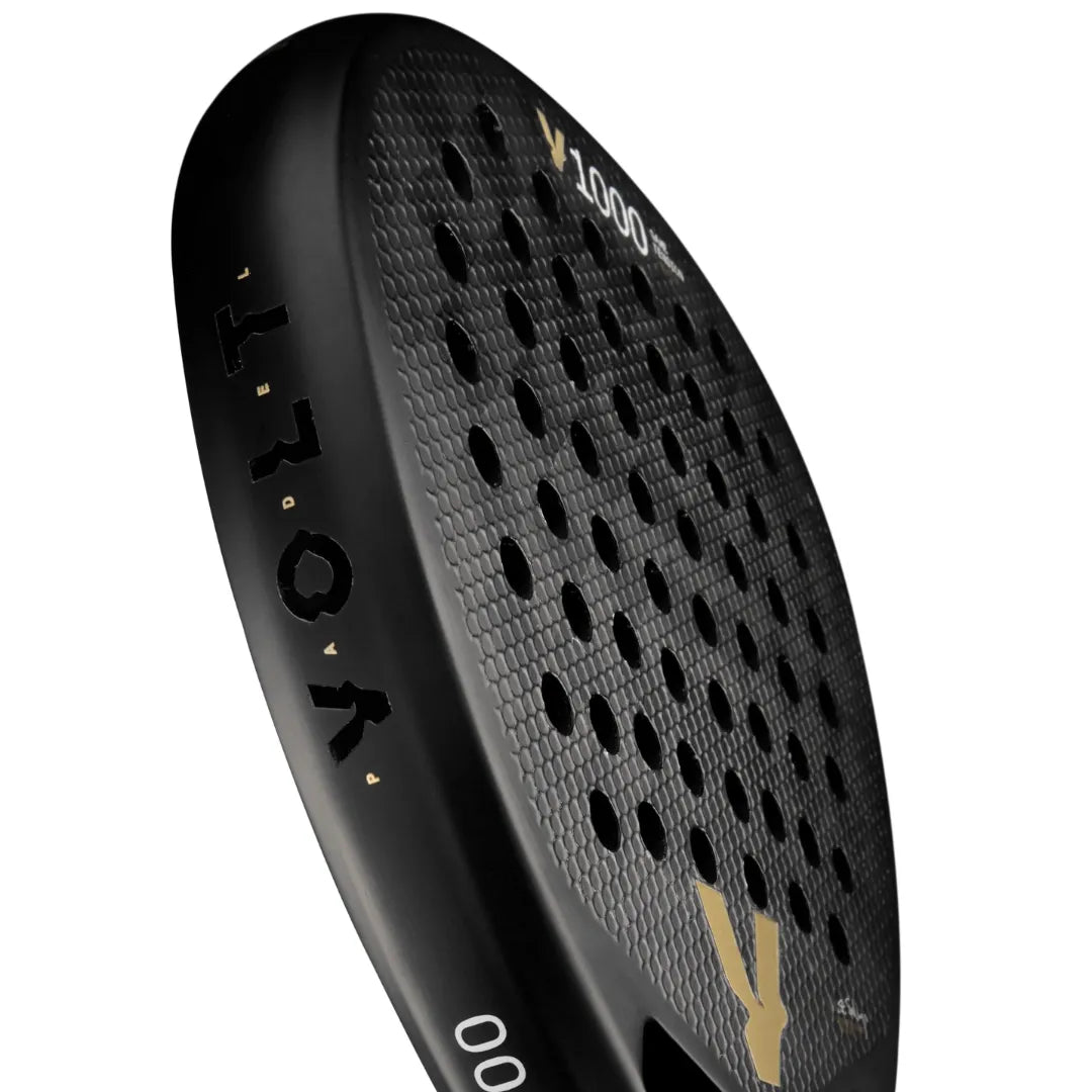 Close-up of a black VOLT 1000 V23 Padel Racket by Volt, showcasing a textured surface and circular holes with VOLO in gold. The diamond-shaped blade suggests an aggressive playing style against a white backdrop.